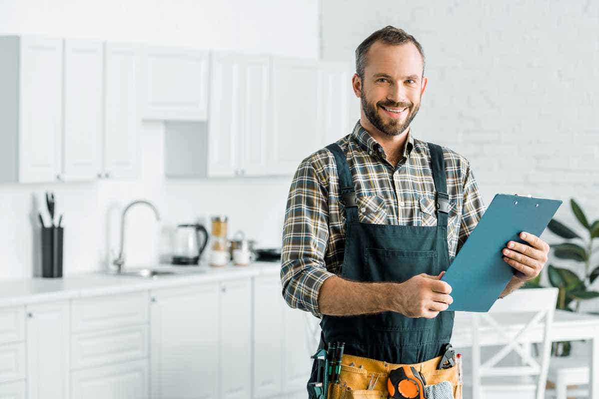Smiling plumber standing in a kitchen, holding a clipboard and looking at the camera