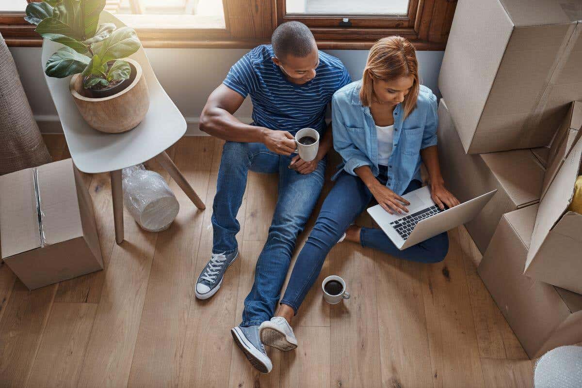 A young couple sits on the floor of their new home shopping for insurance