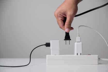 A hand plugging an electric plug into a power strip