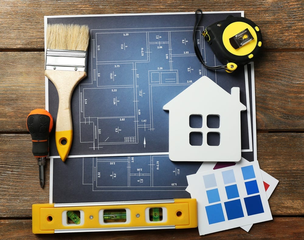 A collection of home remodeling tools: paintbrush, level, measuring tape, plans, and paint samples,