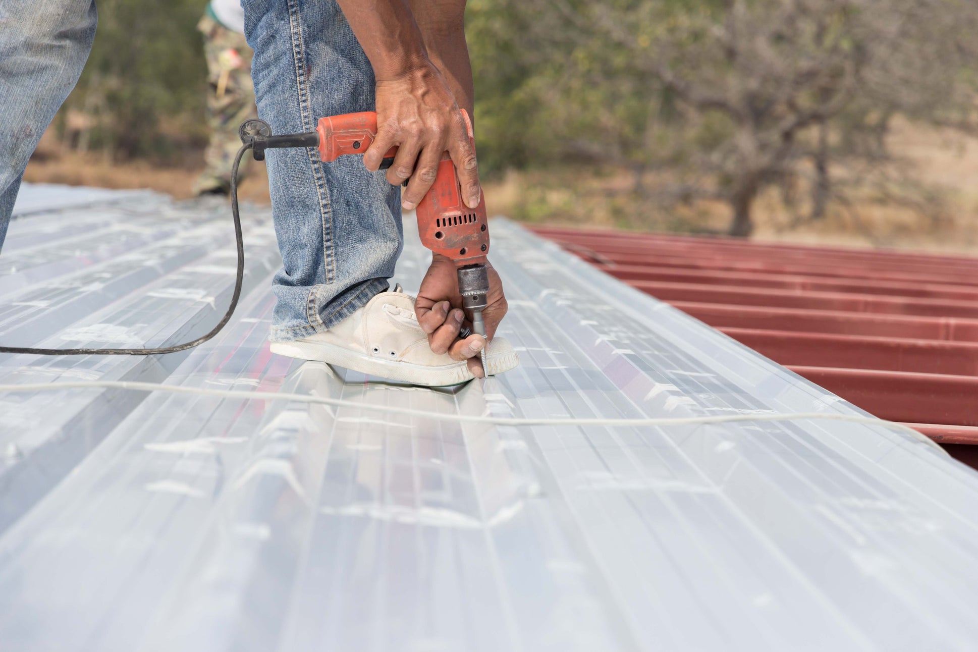 A man stands on a metal roof, drilling a hole