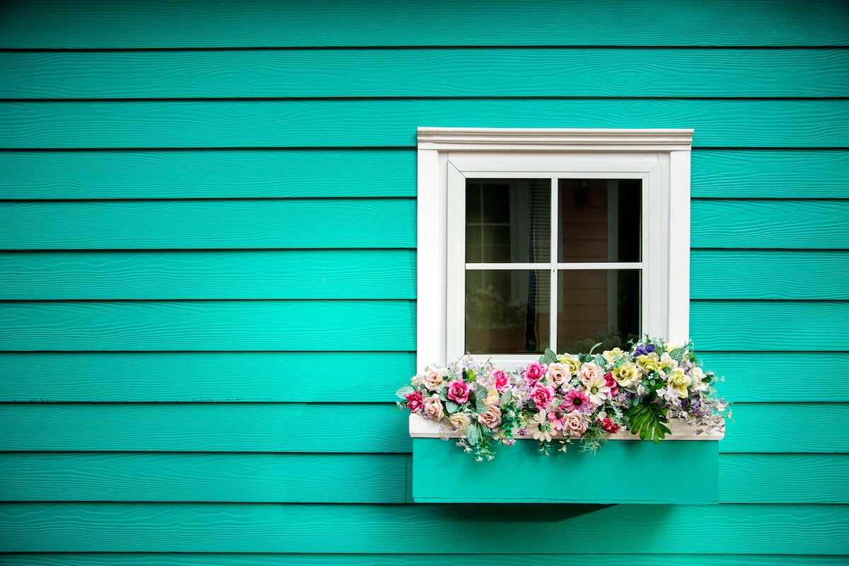 Single white window on teal house with window box full of flowers