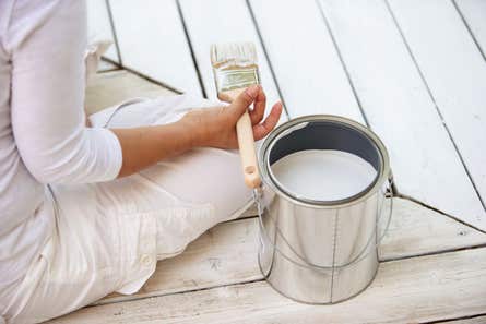 Back-view of woman holding paint brush sitting next to a paint can on deck