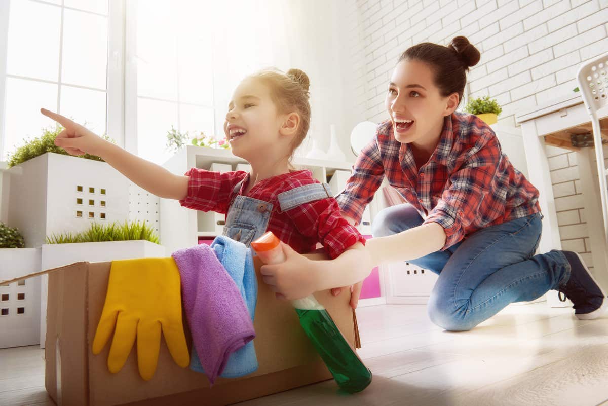 A woman pushes a child in a box with cleaning supplies