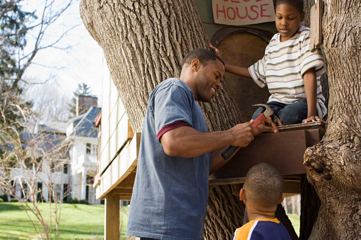 A father helps his two sons build a tree house in their yard