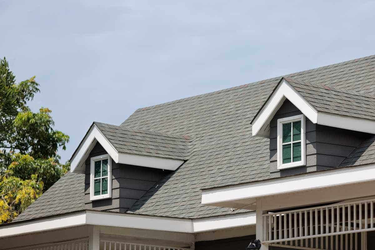 The roof of a house with dark asphalt shinges and two dormers