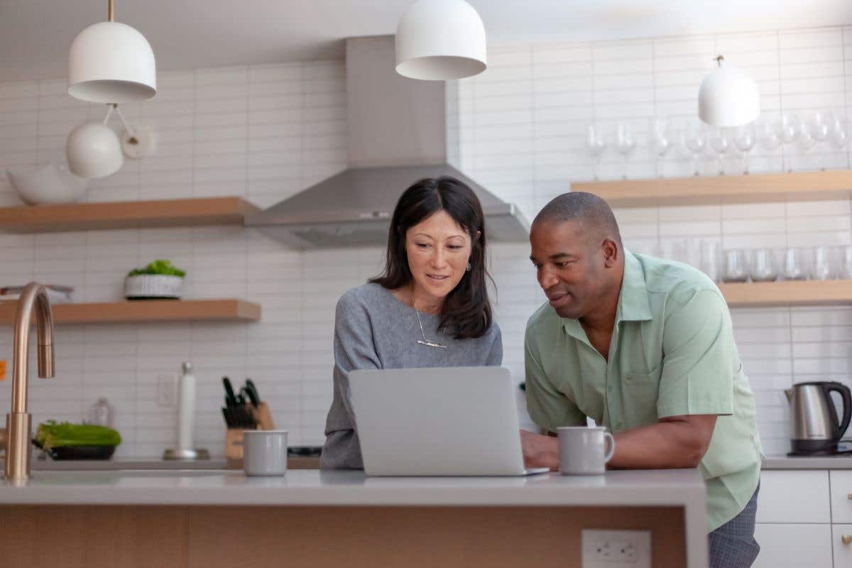 A couple stands at their kitchen island looking at their laptop