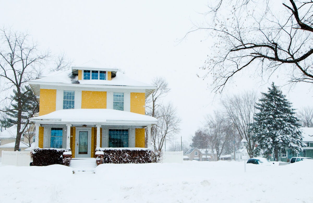 yellow two-story house with a hip shape roof and a snowy front yard