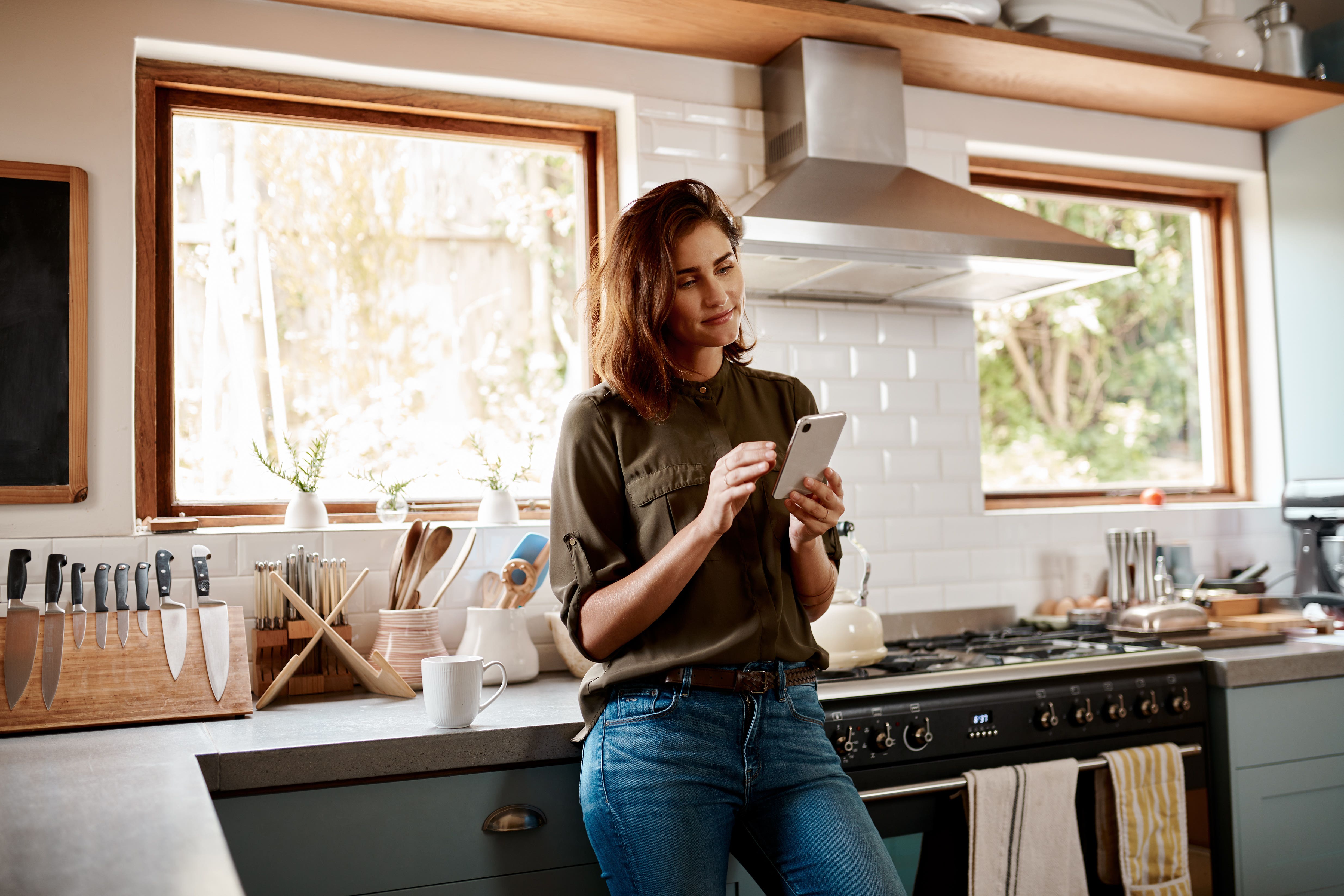 A young woman in the kitchen looking at her phone.