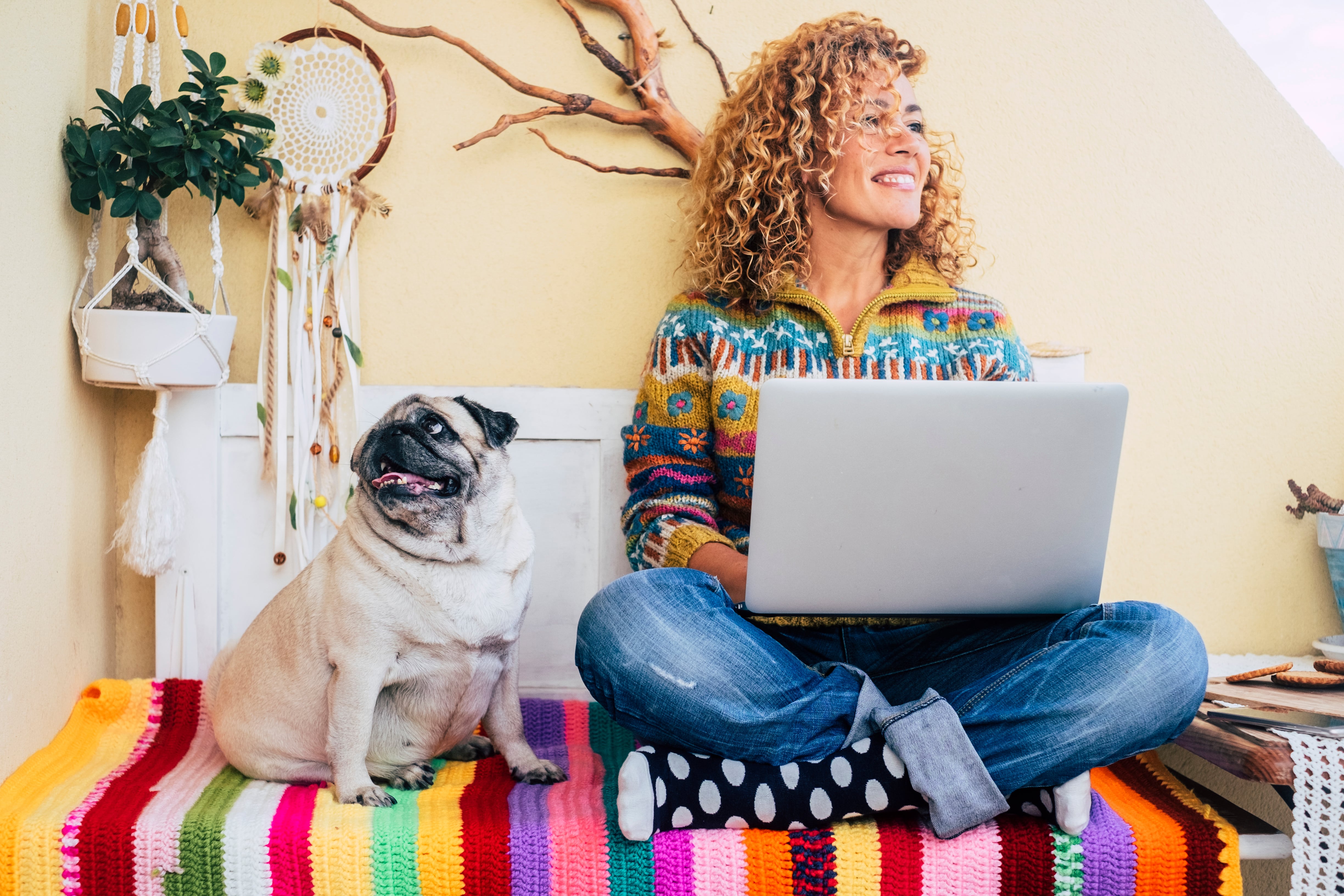 Woman on bed with dog, working from home with a laptop